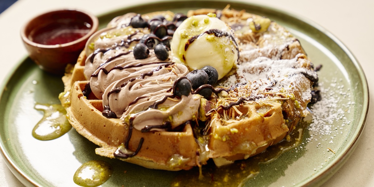Blueberry-topped waffles with butter and drizzled sauces on a green plate at Blueberry's Grill